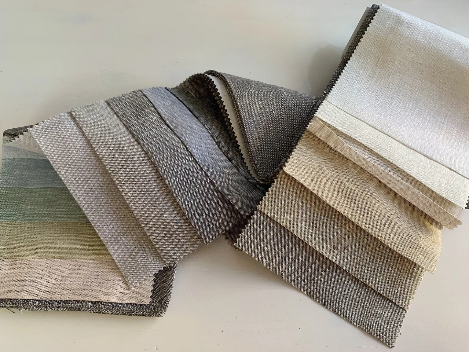 Folded drapery fabric samples in linen and wool stacked on a timber bench